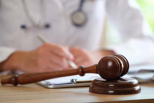 קונספט של תמיכה משפטית באמצעות פטיש עץ של שופט על שולחן רופא שעושה עבודת ניירת ברקע