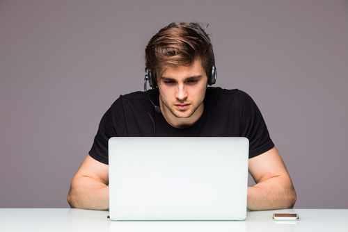 בחור צעיר משחק במחשב נייד לבן עם אוזניות