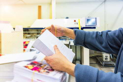 עובד בית דפוס מחזיק מלא ניירות שהדפיס